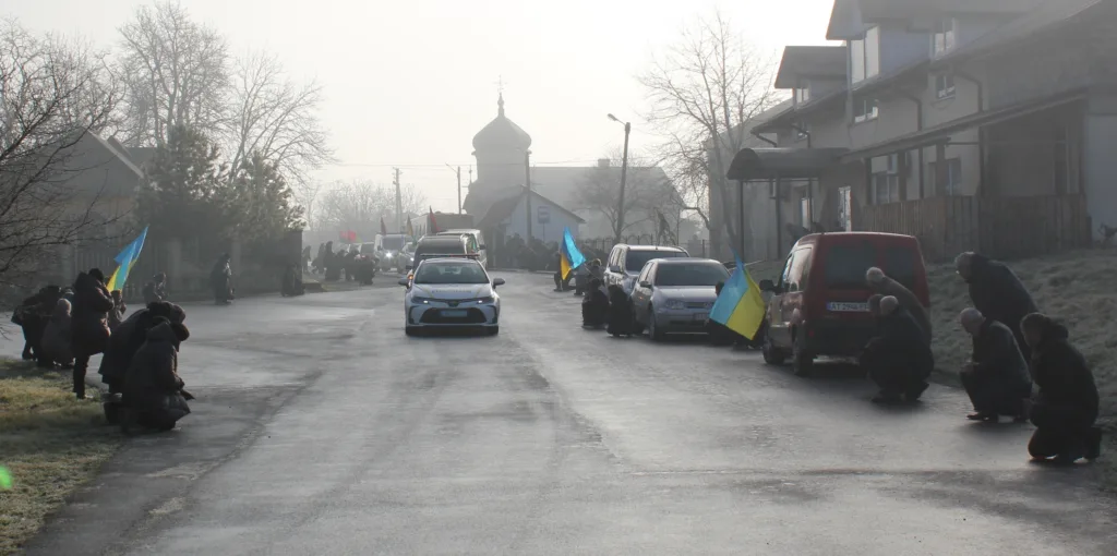 Люди з українськими прапорами стоять вздовж дороги