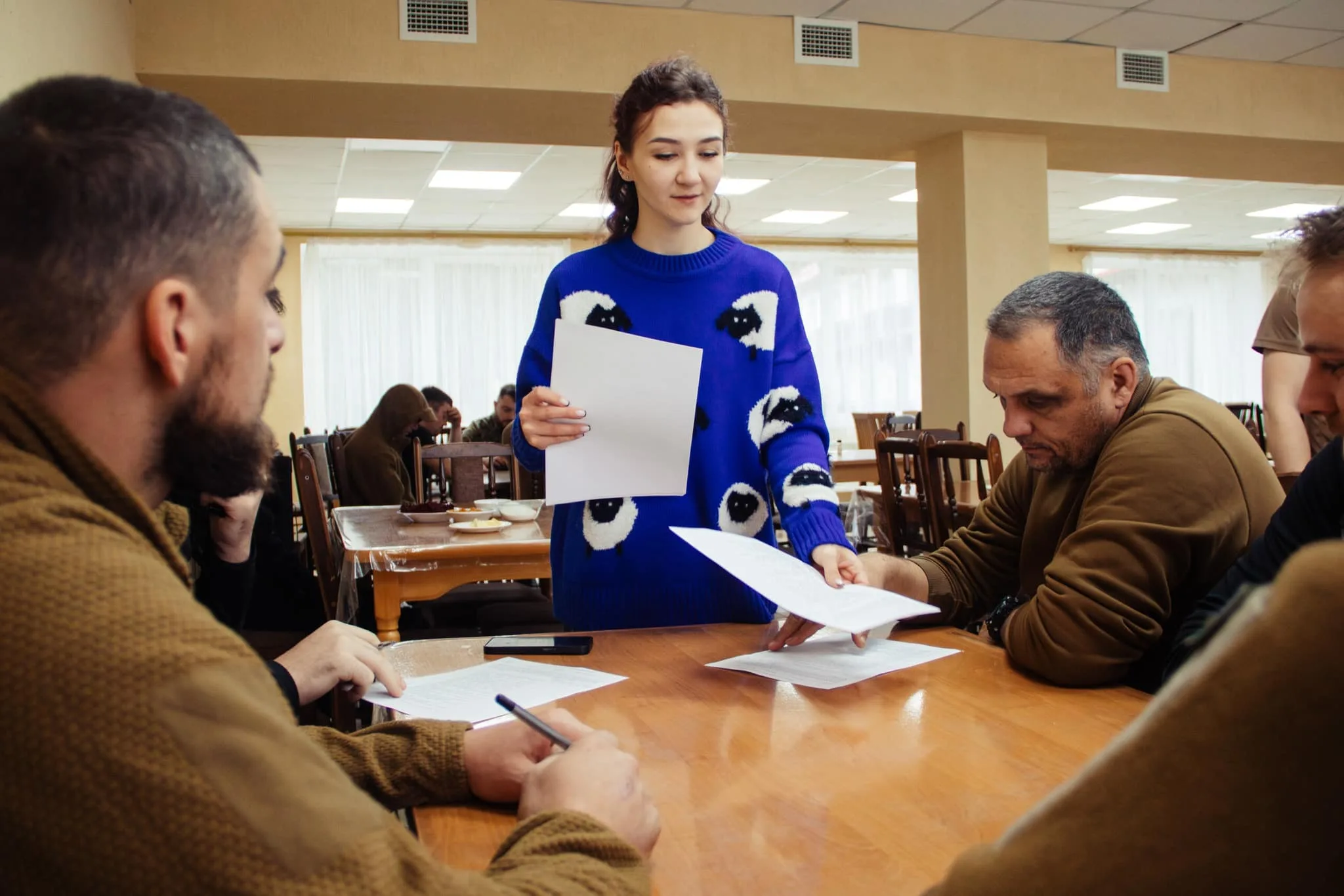 Жінка роздає папери групі людей за столом