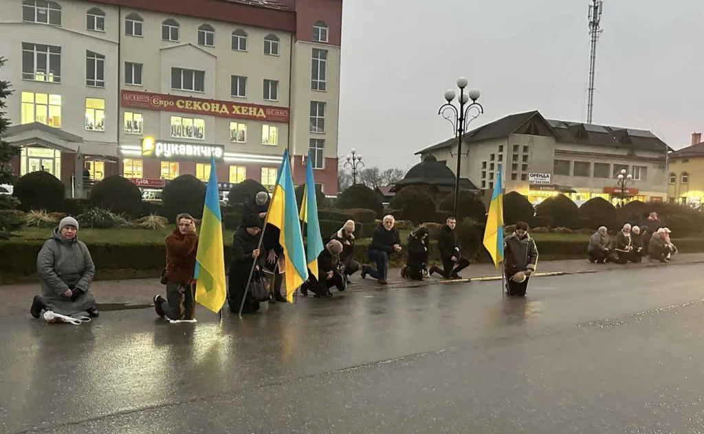 Люди з українськими прапорами стоять на колінах