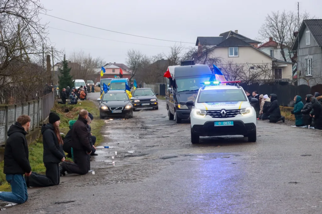 Люди на колінах під час траурної процесії з прапорами