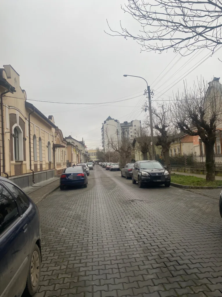 Вузька міська вулиця з припаркованими автомобілями