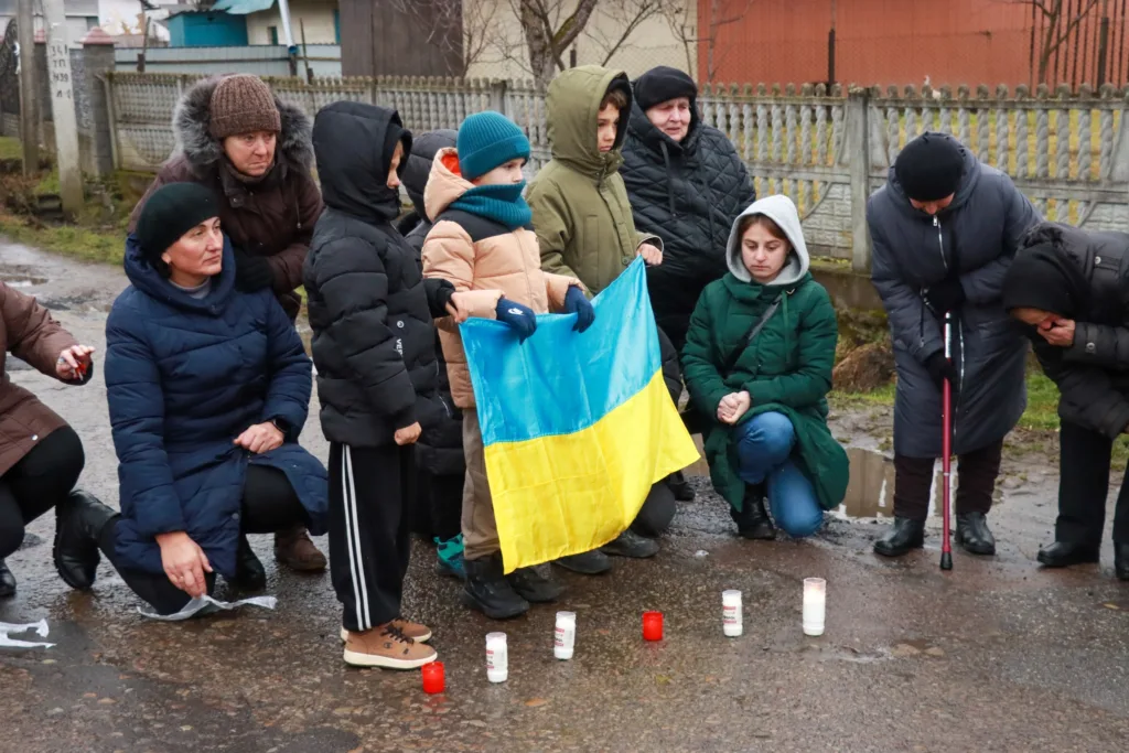 Люди з українським прапором запалюють свічки пам’яті