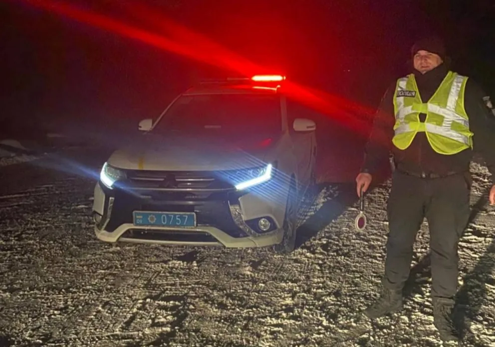 Поліцейський біля патрульного авто вночі