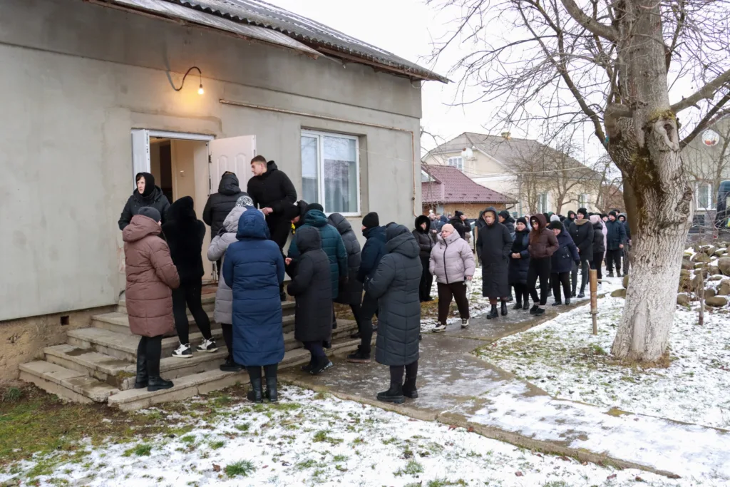 Люди стоять у черзі біля будівлі взимку