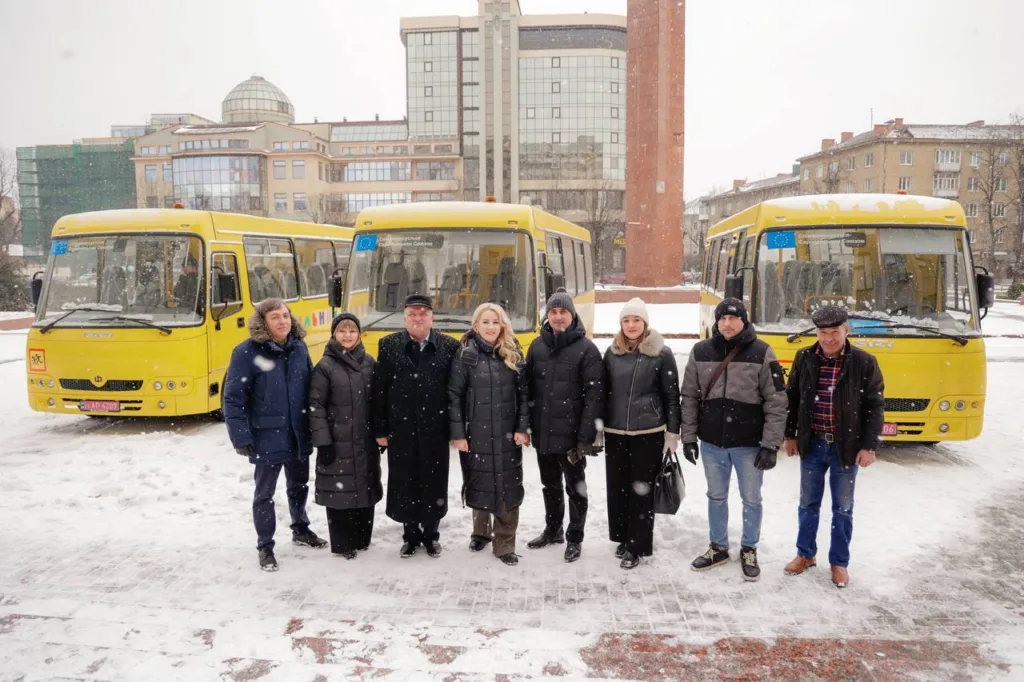 Люди стоять перед жовтими автобусами взимку