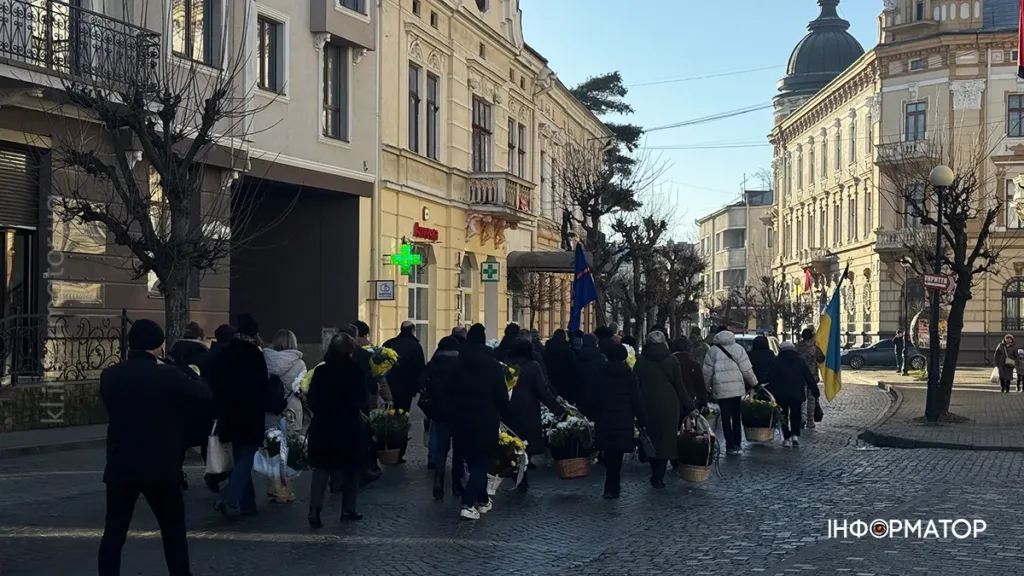 Люди з квітами йдуть вулицею українського міста