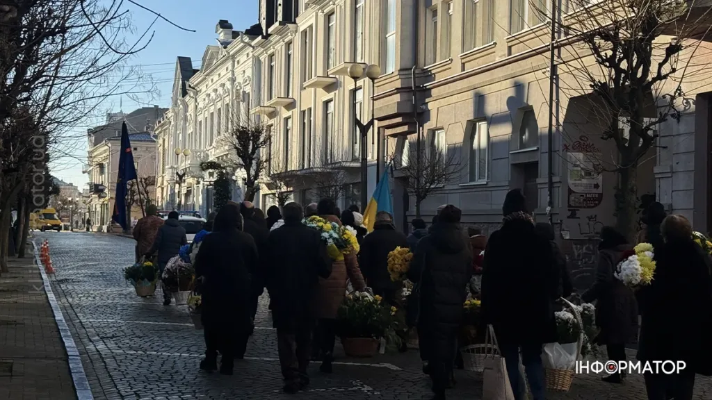 Люди йдуть вулицею з квітами та прапорами