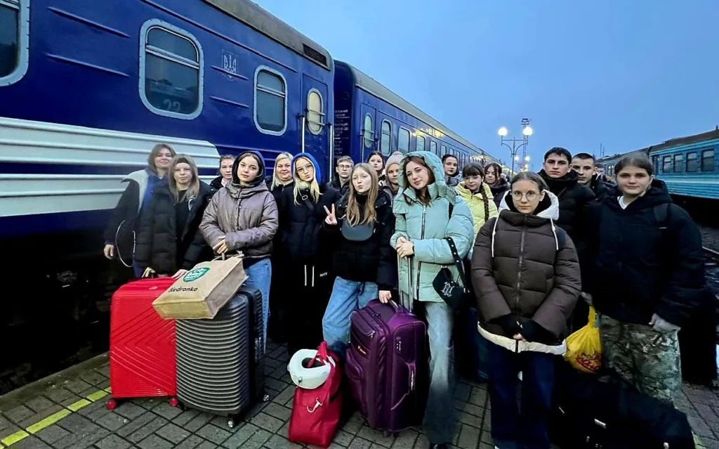 Група людей з валізами біля поїзда на вокзалі