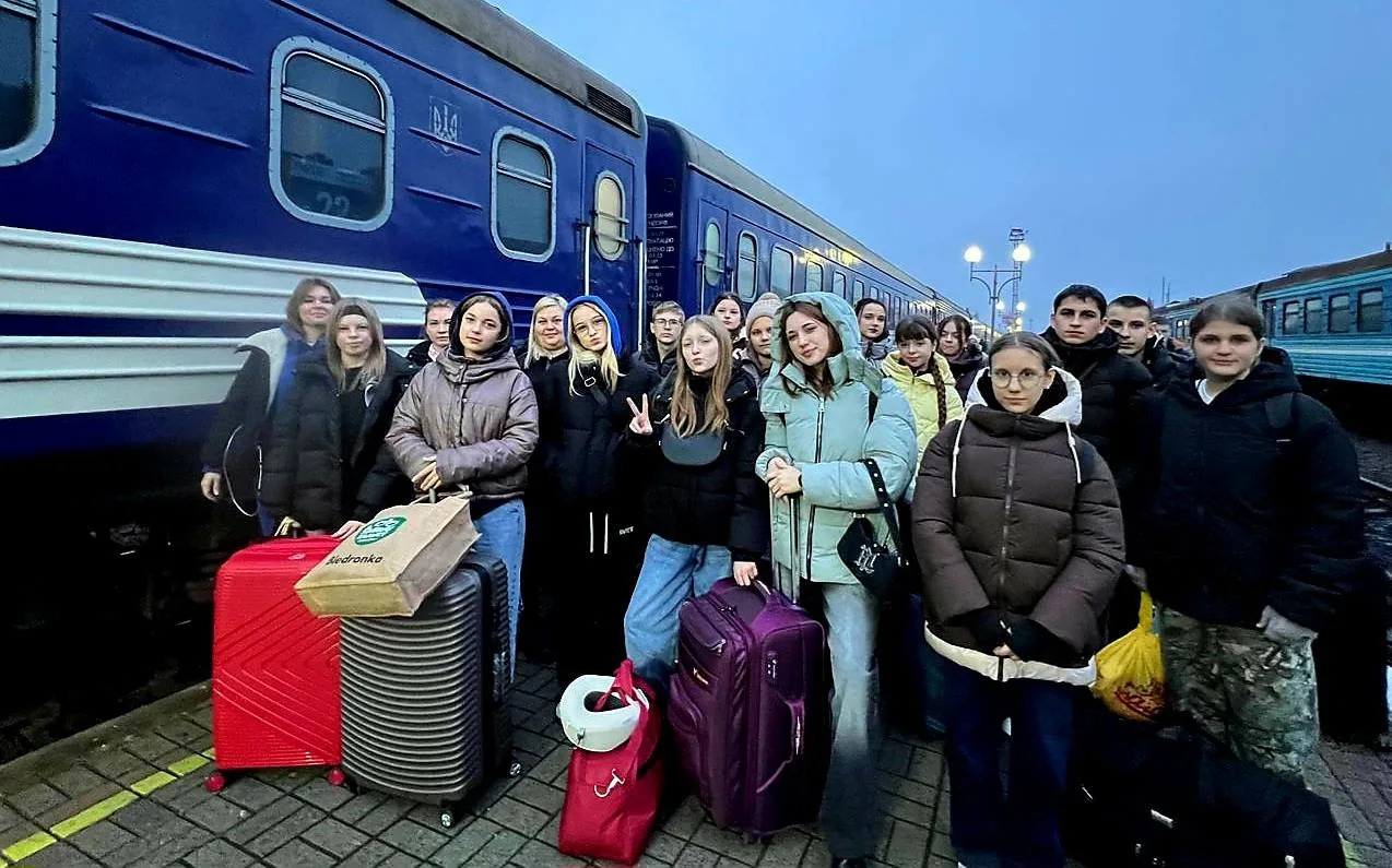 Група людей з валізами біля поїзда на вокзалі