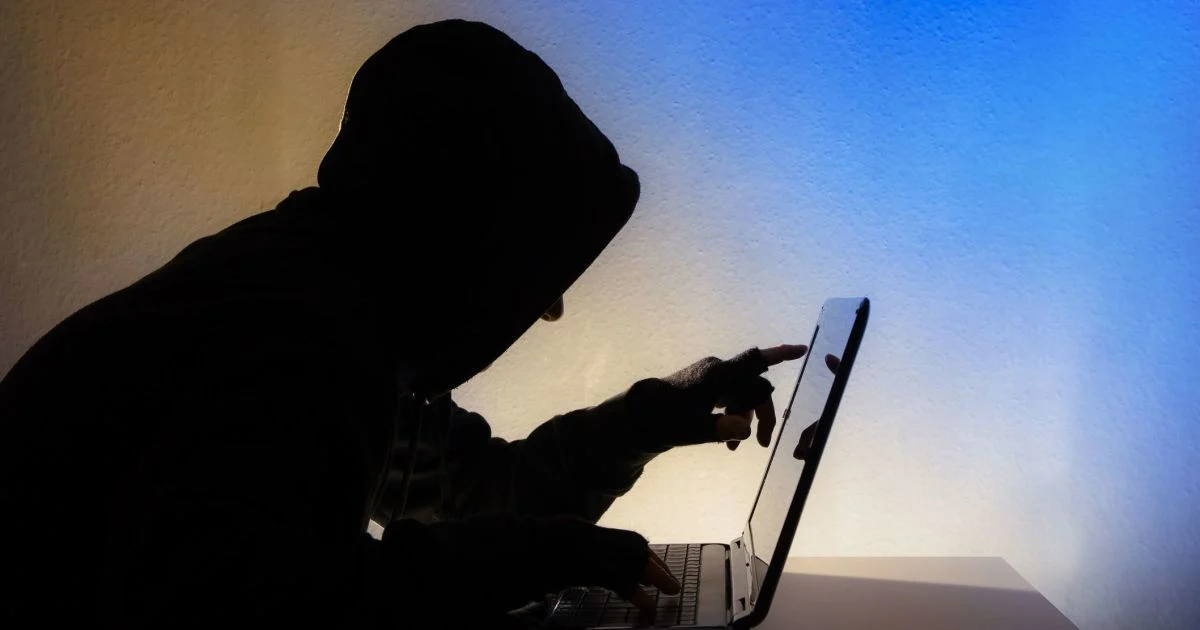 Хакер у темній худі працює за ноутбуком
