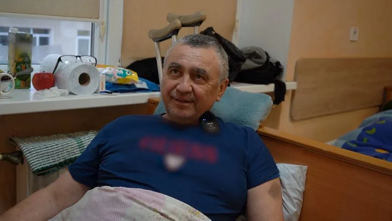 Чоловік усміхається, лежачи в лікарняному ліжку