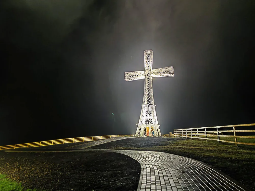 Освітлений металевий хрест уночі на пагорбі