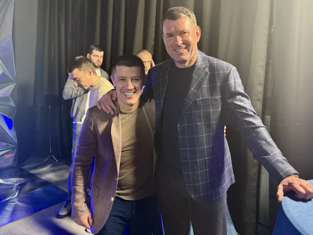 Двоє чоловіків посміхаються на сцені з освітленням