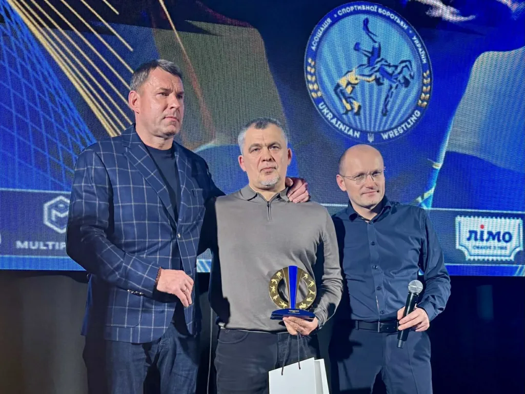 Троє чоловіків на церемонії нагородження з трофеєм