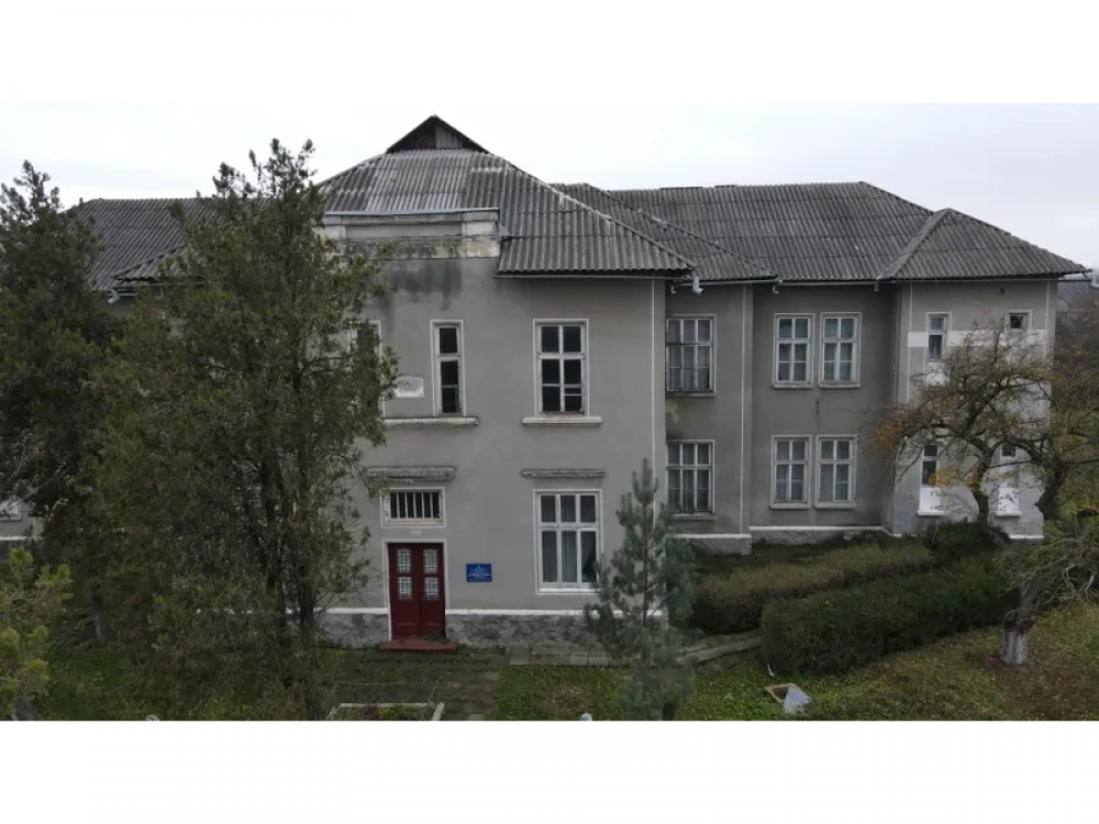 Сірий двоповерховий будинок серед дерев восени