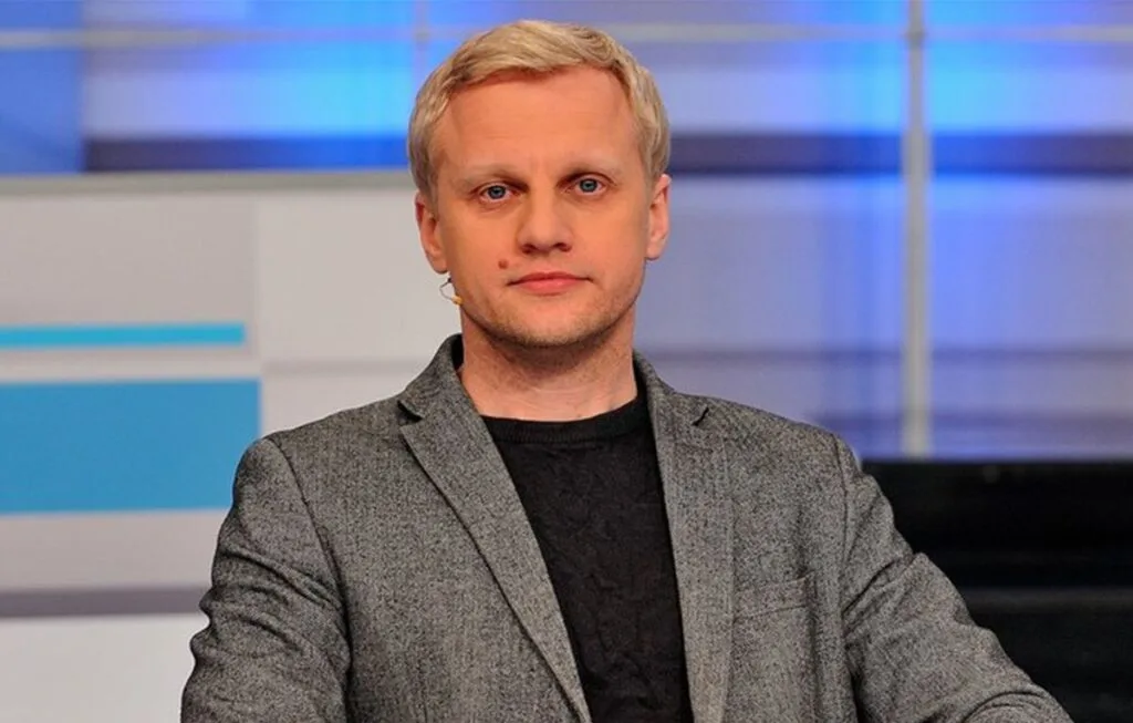 Чоловік у сірому піджаку сидить у студії