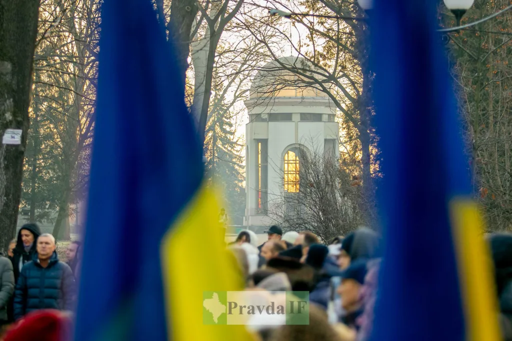 Люди з українськими прапорами біля пам'ятника