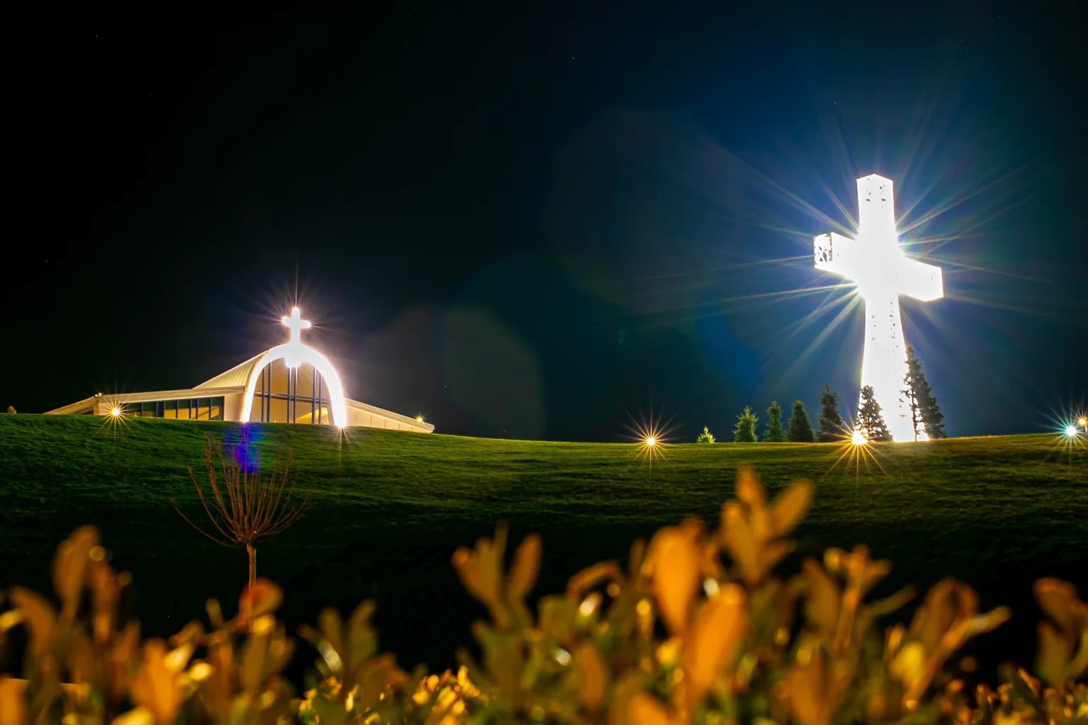 Освітлений хрест і церква вночі на пагорбі