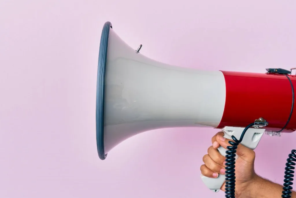 Рука тримає червоно-білий мегафон на рожевому фоні