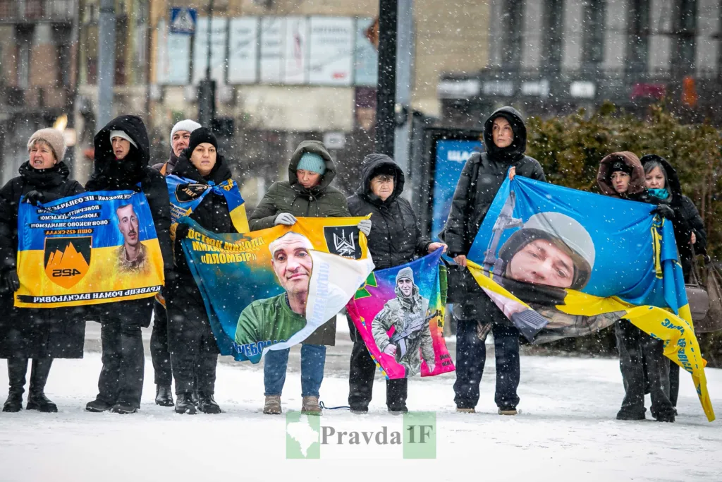 Люди тримають прапори з фотографіями військових на снігу