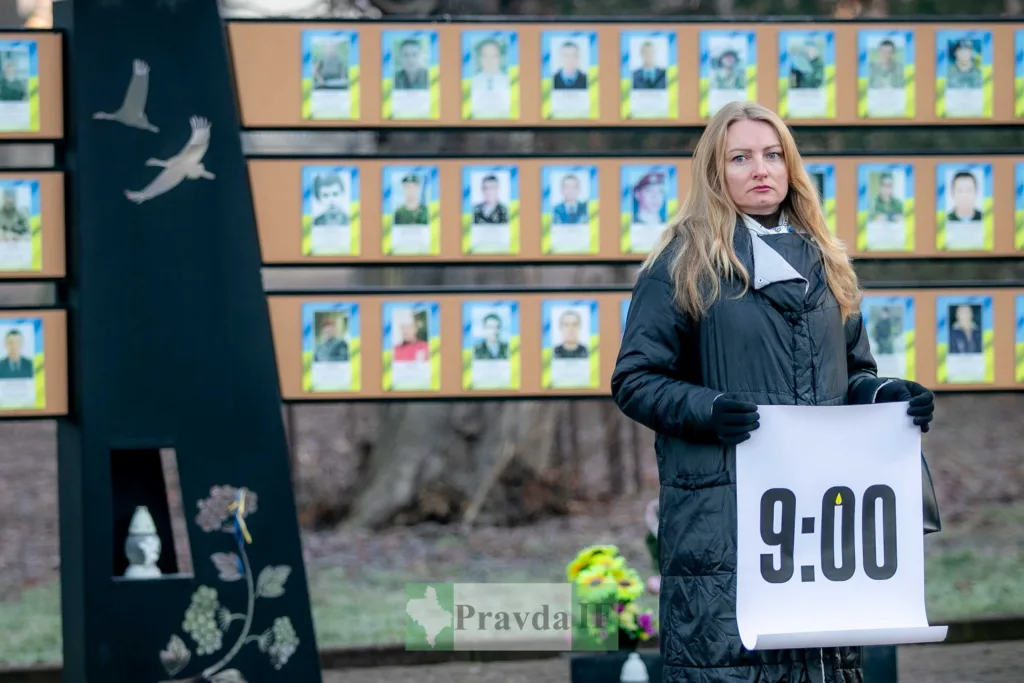 Жінка тримає плакат перед меморіалом героїв