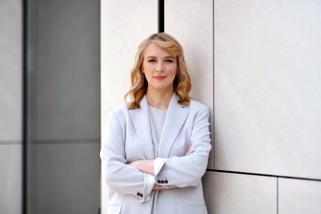 Жінка у світлому костюмі стоїть біля стіни