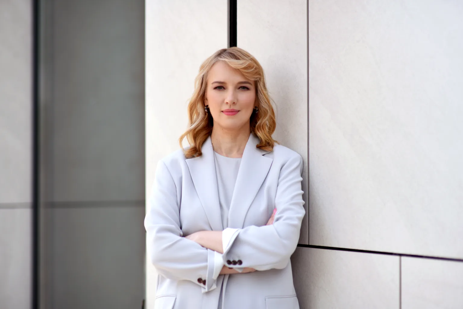 Жінка у світлому костюмі стоїть біля стіни