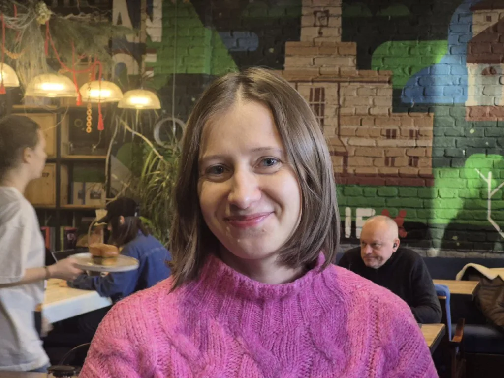 Жінка у рожевому светрі в кафе