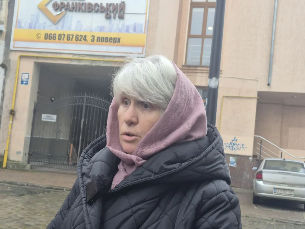 Жінка в куртці стоїть біля будівлі