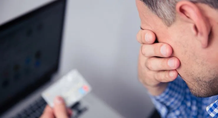 Засмучений чоловік із кредитною карткою біля ноутбука