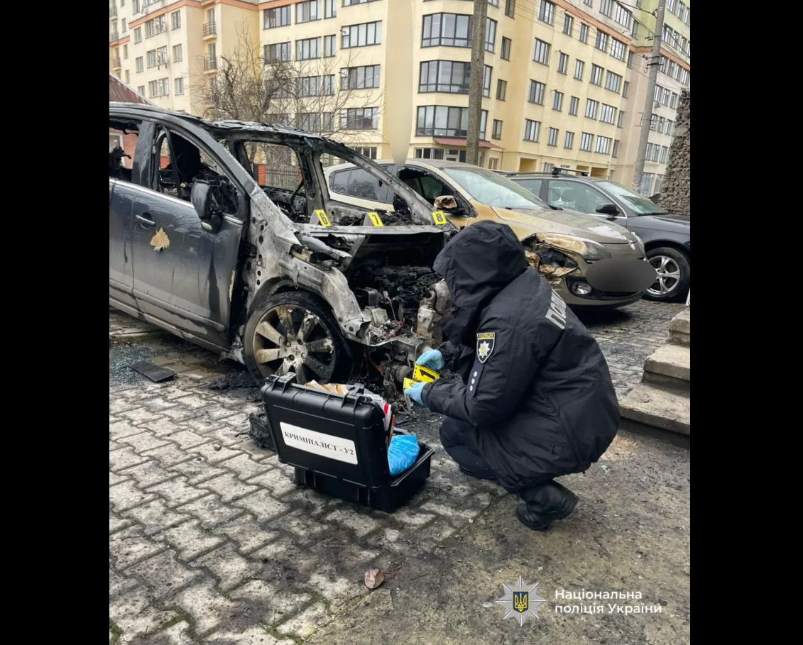 Поліцейський оглядає згорілий автомобіль на парковці