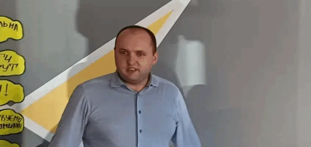 Чоловік виступає перед аудиторією біля стіни