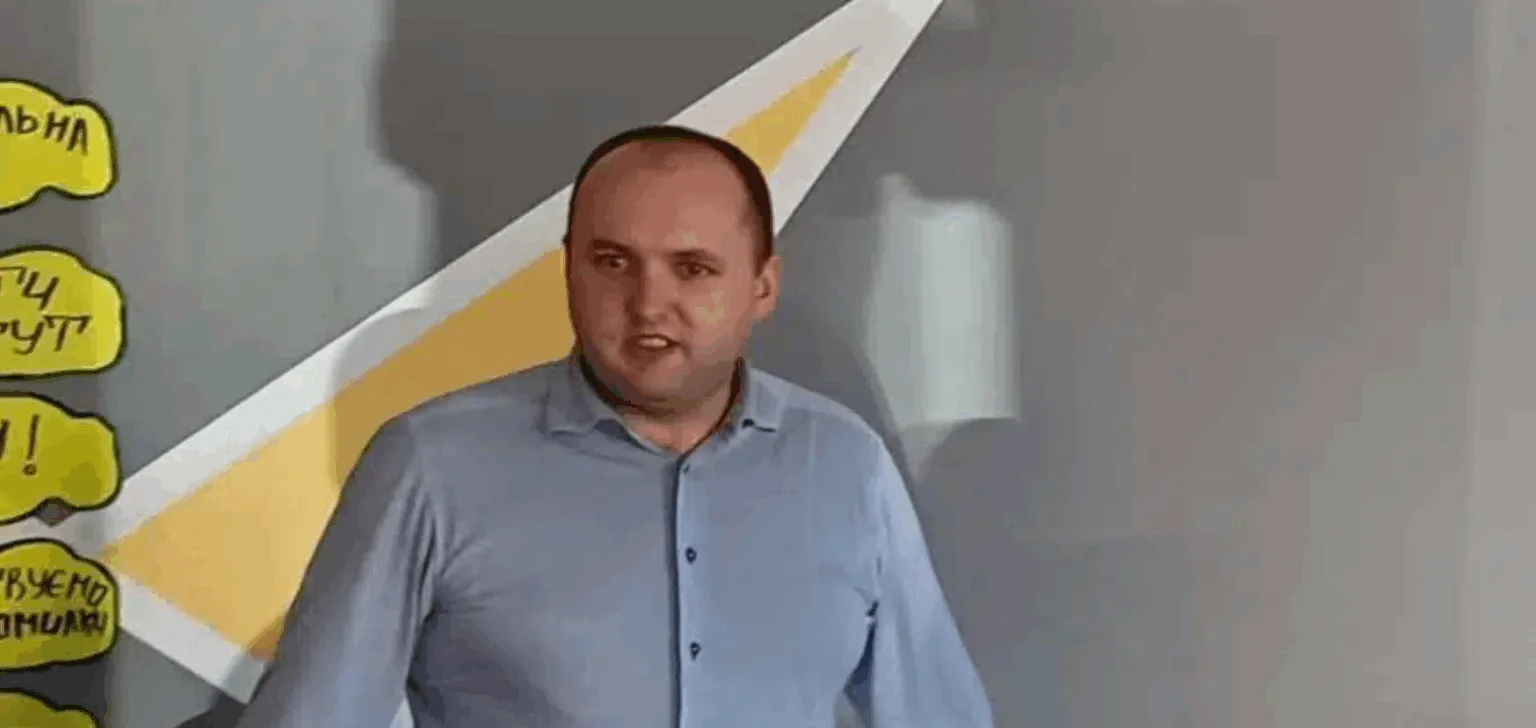 Чоловік виступає перед аудиторією біля стіни