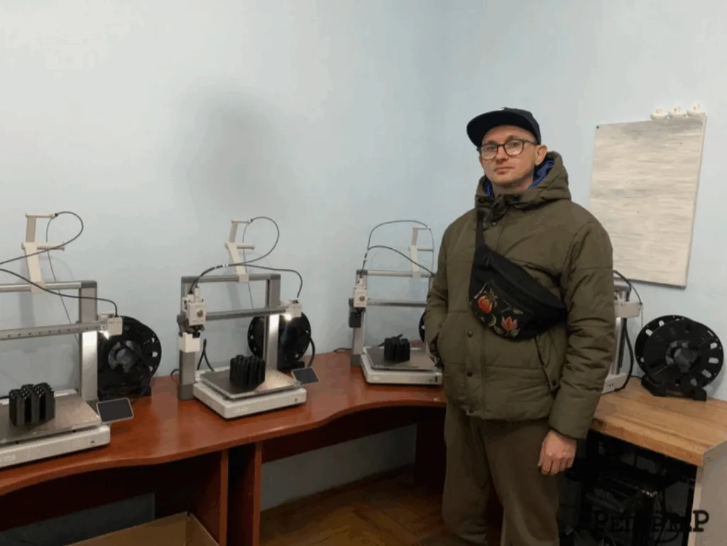 Людина стоїть біля трьох 3D-принтерів у кімнаті
