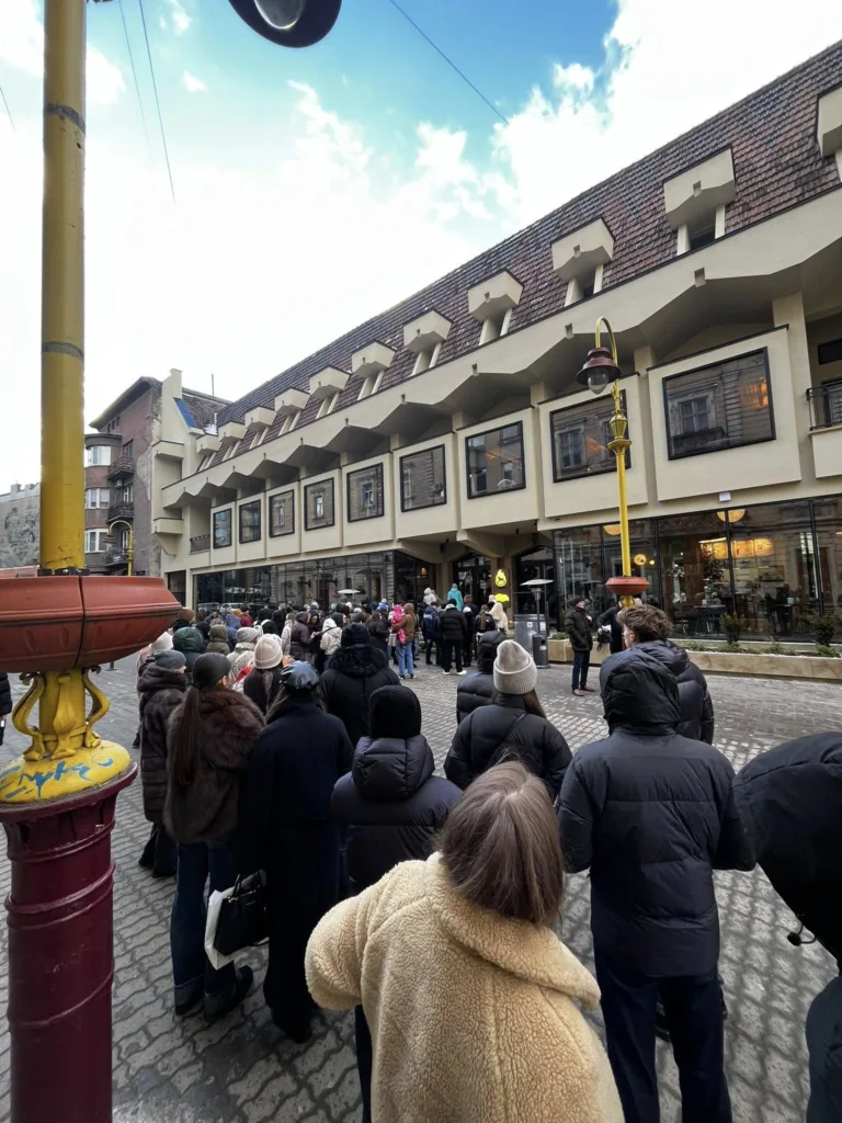 Люди стоять у черзі біля сучасної будівлі