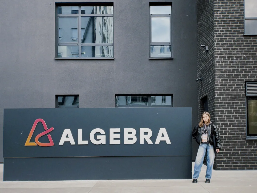 Жінка стоїть біля будівлі з написом Algebra