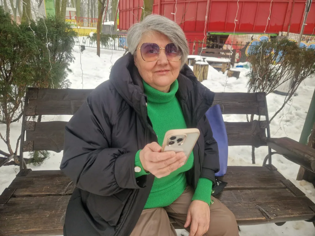 Жінка сидить на лавці зі смартфоном взимку