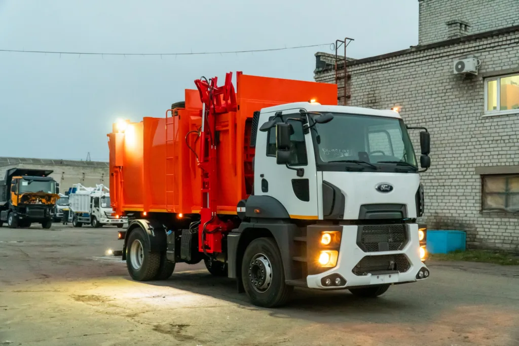 Помаранчева вантажівка-сміттєвоз на заводському подвір’ї