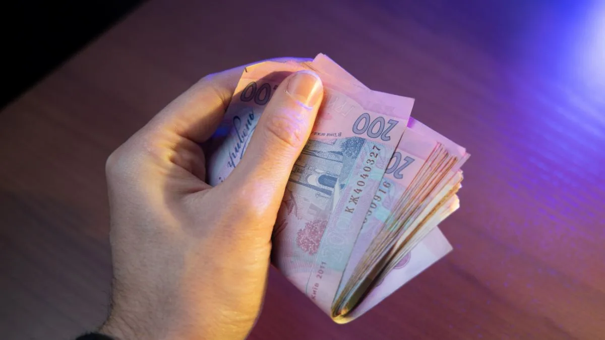 Рука тримає купюри двісті гривень