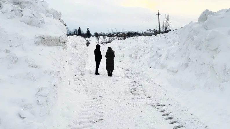 Двоє людей йдуть засніженою дорогою між заметами