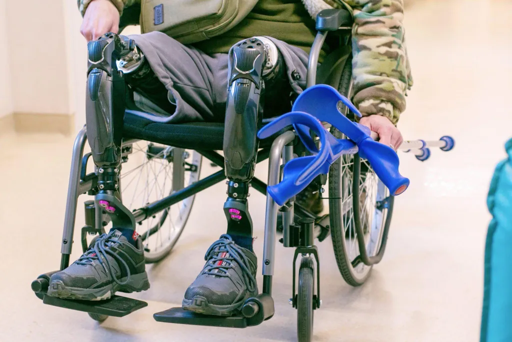 Людина у візку з протезами ніг та милицями