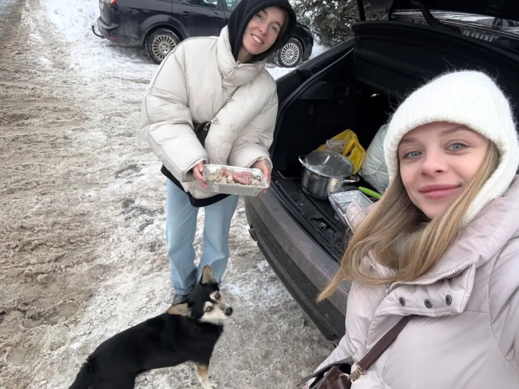 Дві жінки на снігу годують собаку біля авто