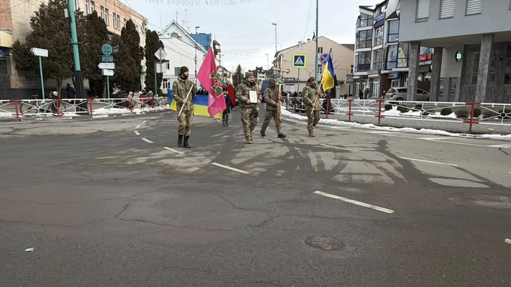 Військові несуть прапори та хрест вулицею міста