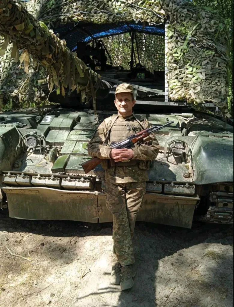 Військовий перед замаскованим танком у лісі