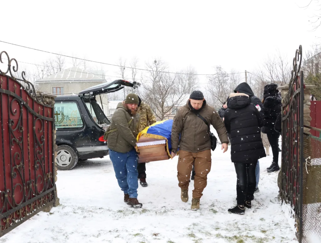 Люди несуть труну, покриту українським прапором взимку