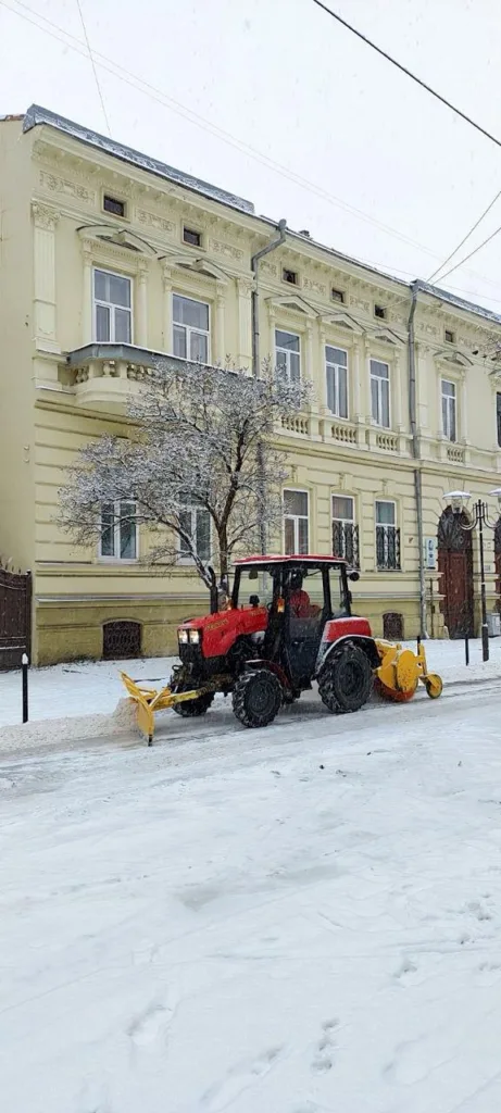 Трактор чистить сніг біля старої будівлі