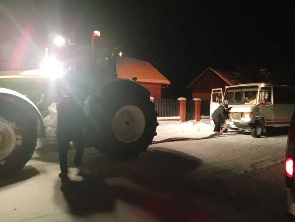 Трактор тягне мікроавтобус зі снігу вночі