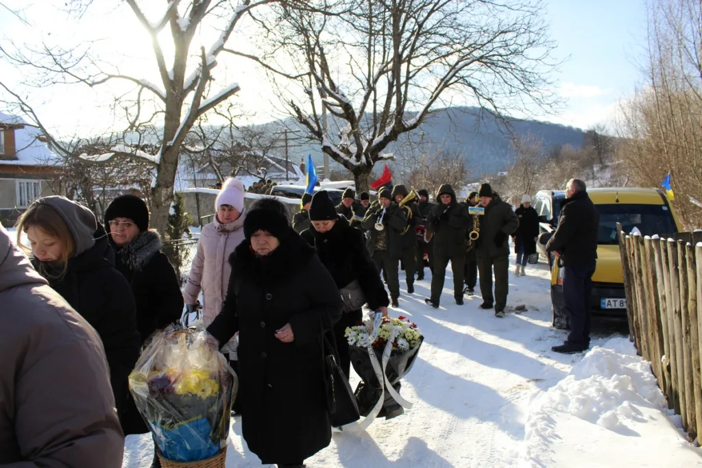 Люди з квітами на зимовій похоронній процесії