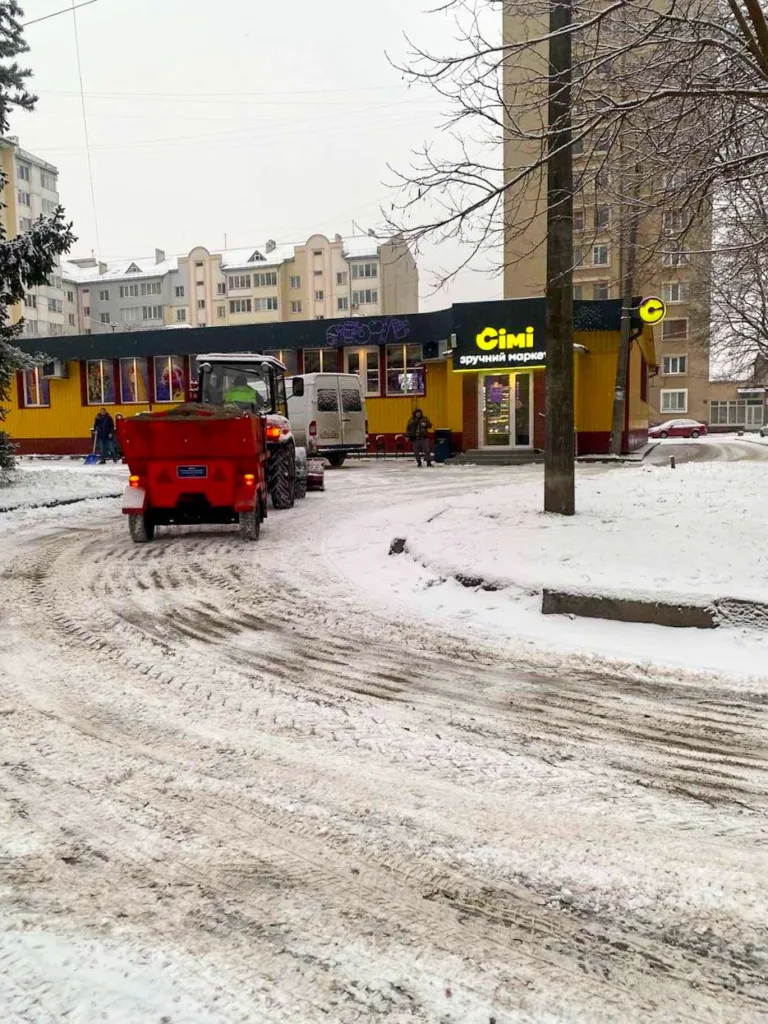 Трактор чистить сніг біля магазину взимку