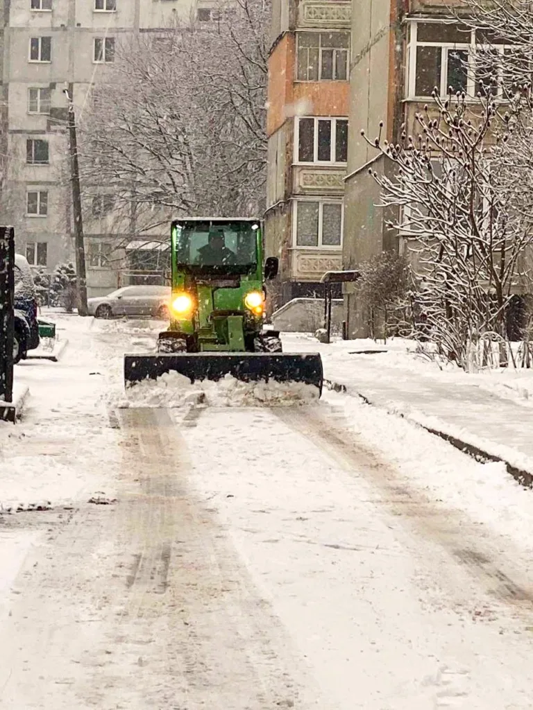 Трактор прибирає сніг біля житлового будинку